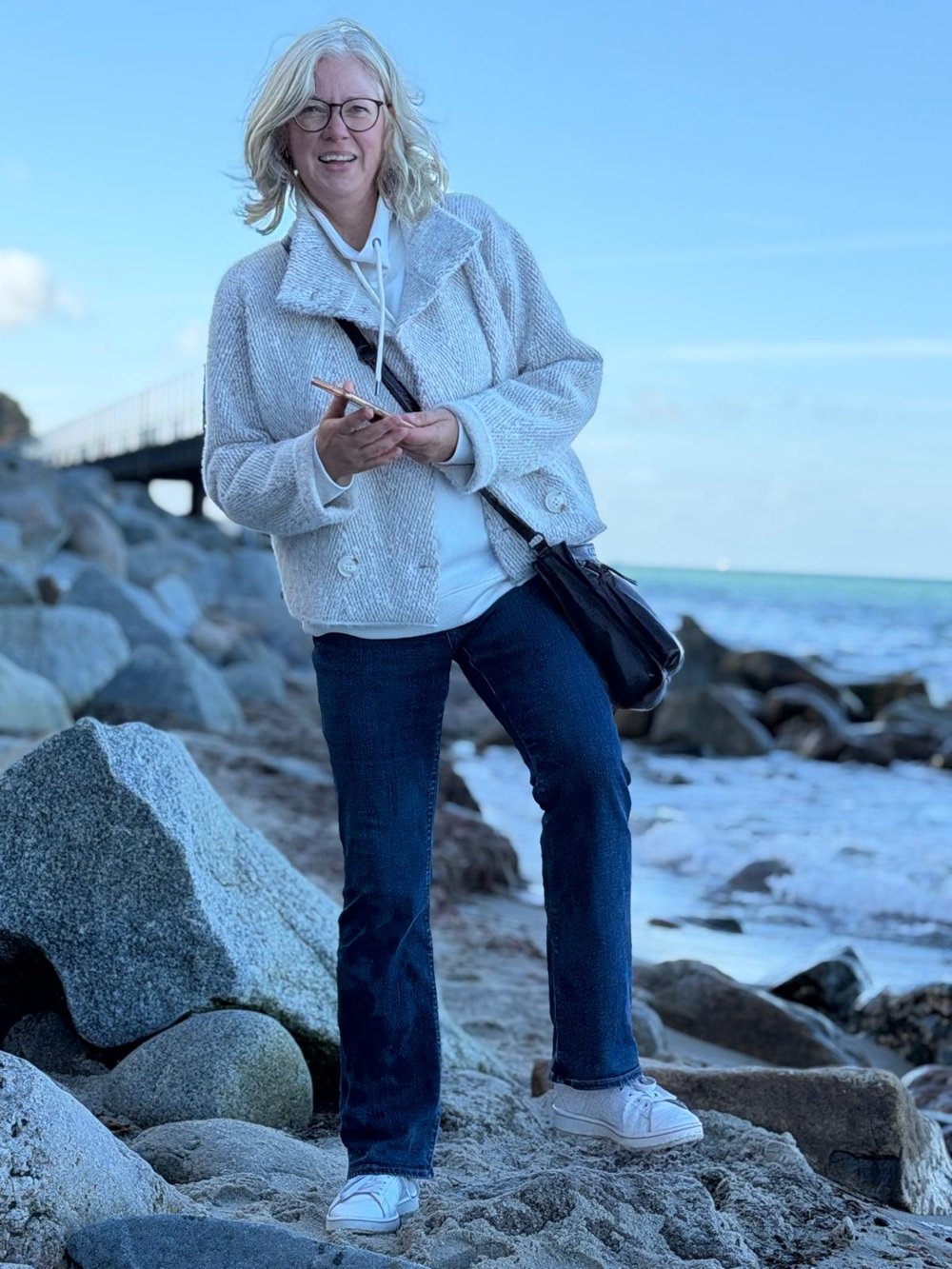 Antje Walsemann am Strand zwischen Steinen, im Hintergrund eine Seebrücke